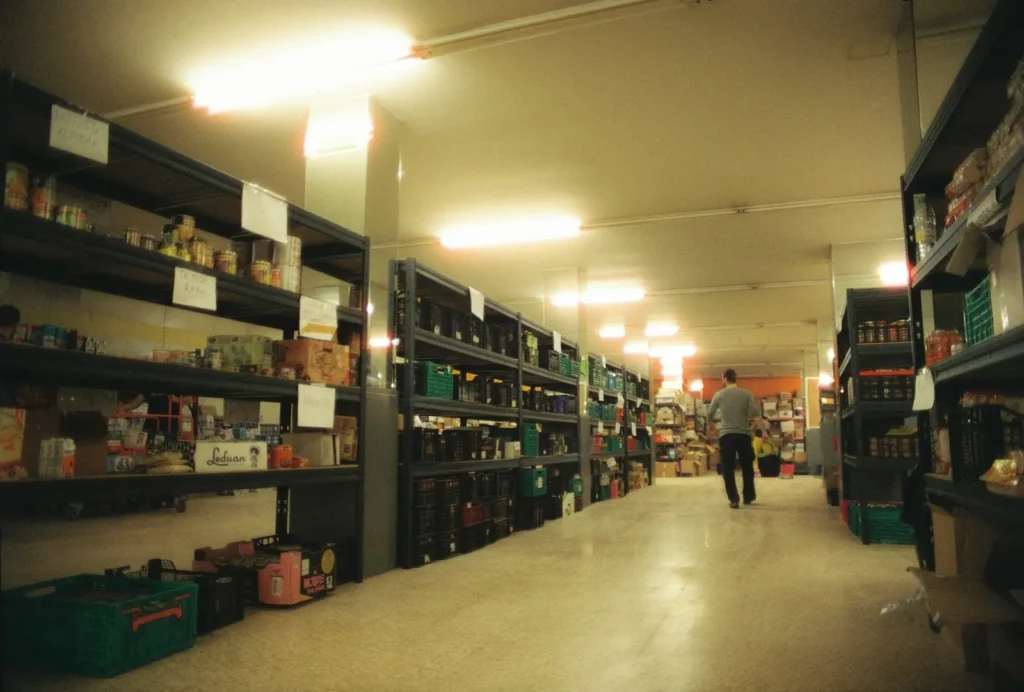 Pasillo de un almacén de alimentación en Alfafar con estanterías de conservas, cajas y un operario al fondo
