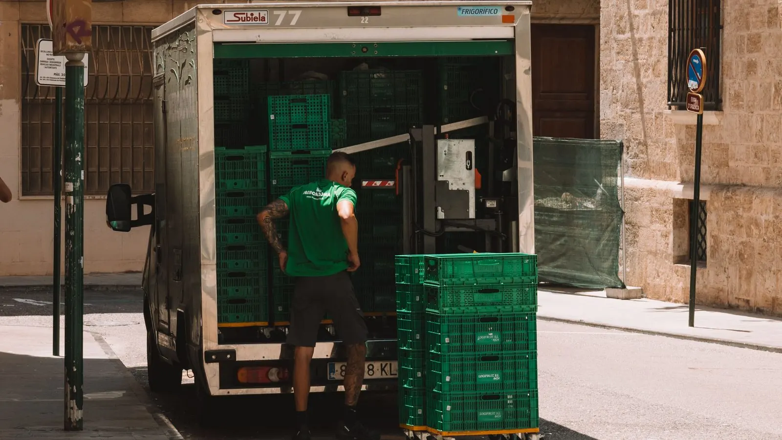 Repartidor descargando cajas verdes de un camión frigorífico en una calle de Valencia