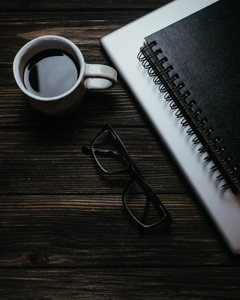 Mesa de madera con una taza de café, unas gafas y un cuaderno
