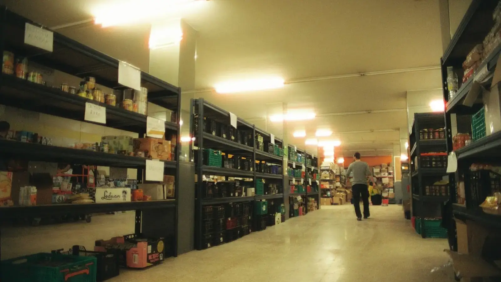 Pasillo de un almacén de alimentación en Alfafar con estanterías de conservas, cajas y un operario al fondo