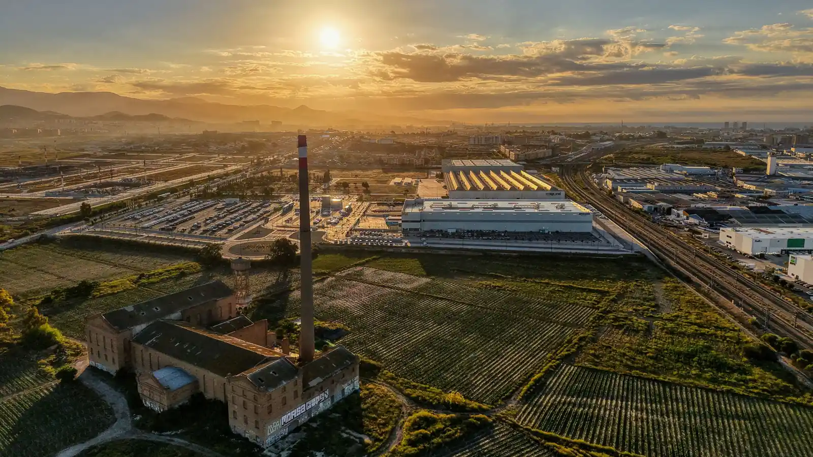 Polígono industrial de Málaga al atardecer, con naves logísticas, vías de tren y campos de cultivo