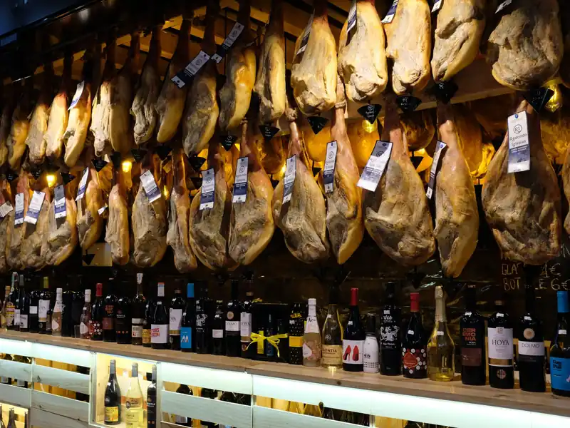 Jamones colgados sobre una fila de botellas de vino español en una tienda de Barcelona